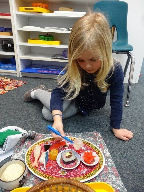 Young girl playing with toy sushi, using chopsticks