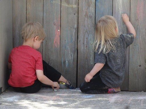 Two children drawing with chalk on a wooden fence, outdoors