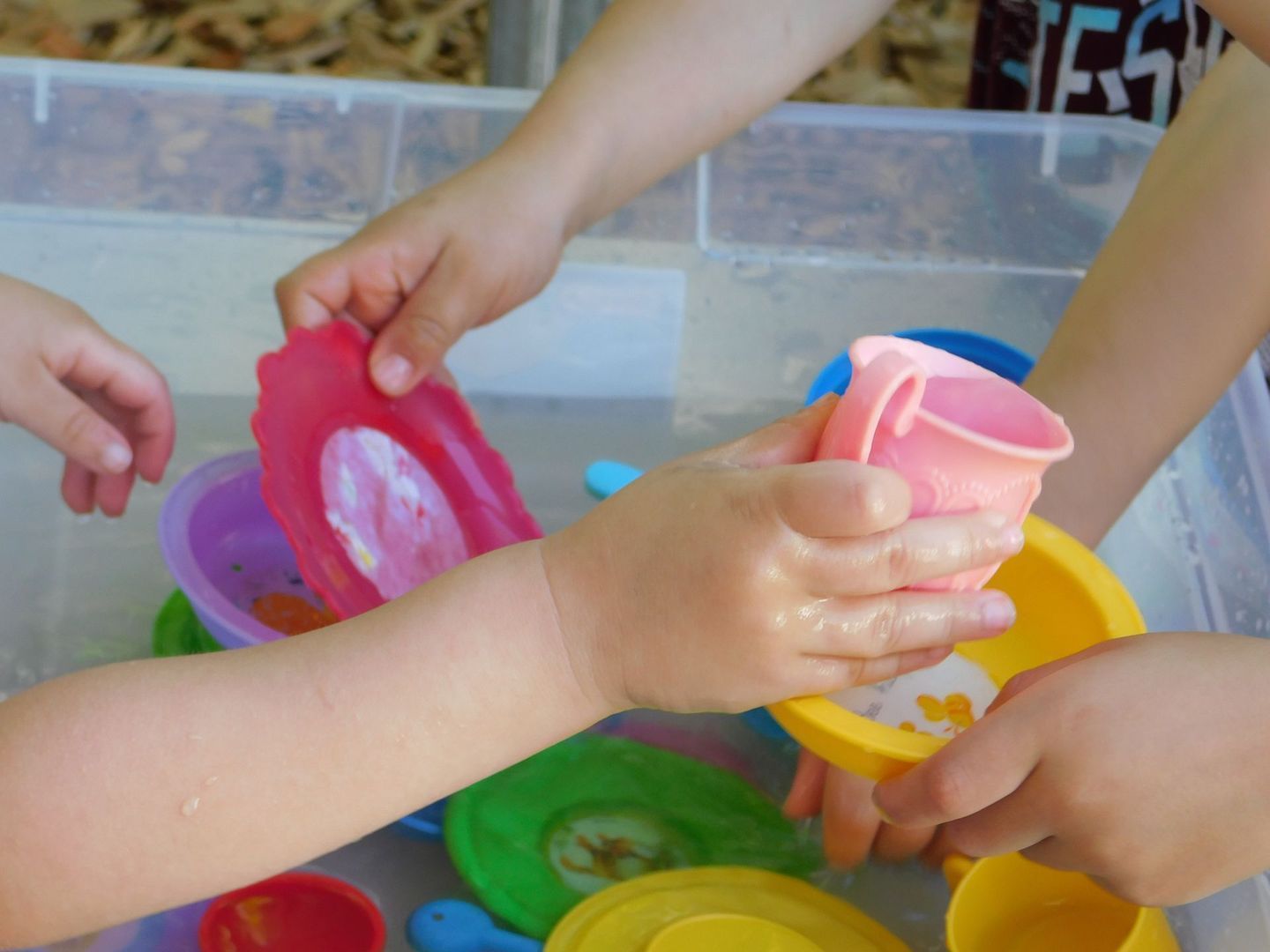 Children's hands playing with colorful plastic bowls in a water-filled bin