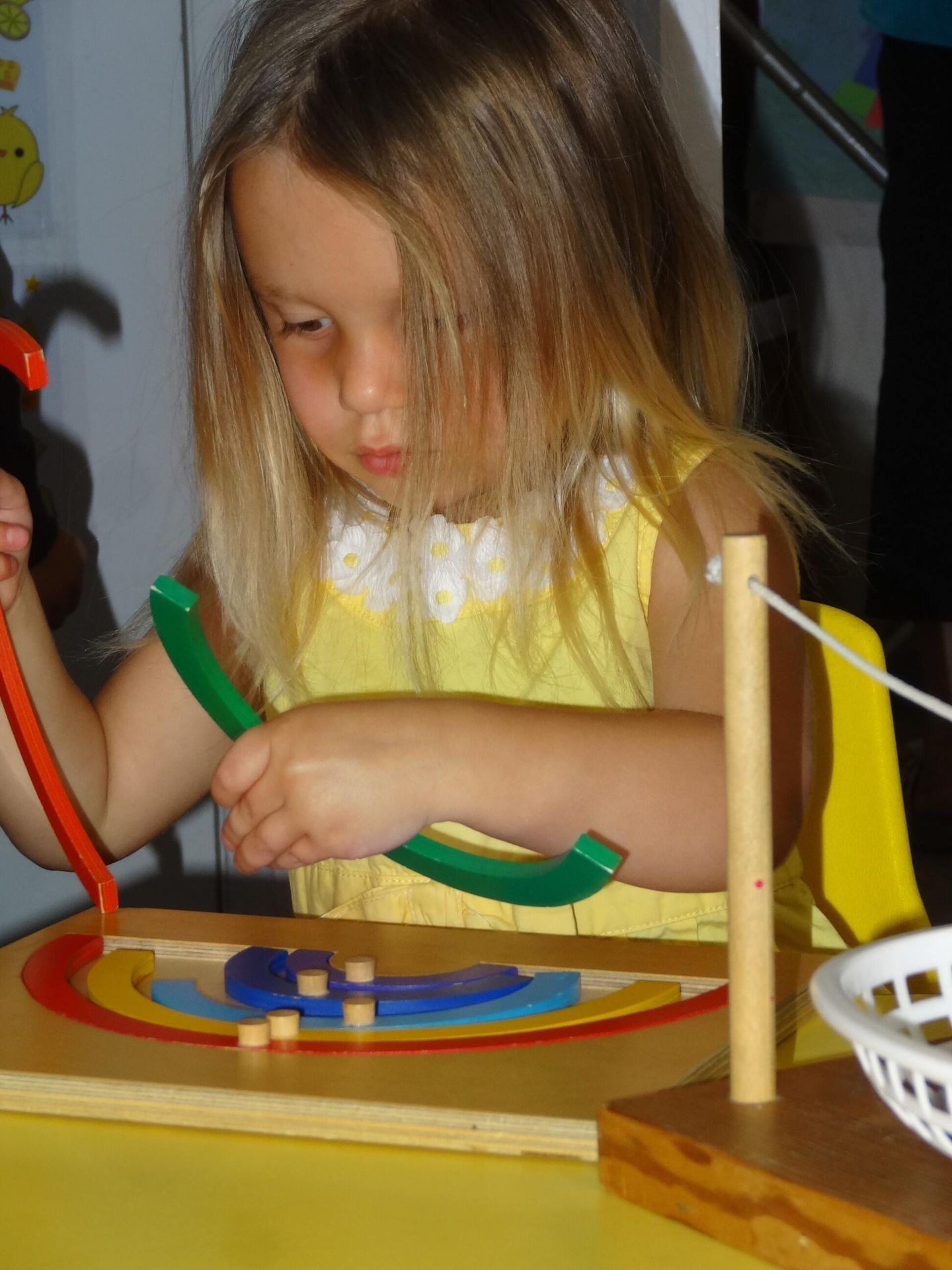 Girl with blonde hair focused on a rainbow puzzle, indoors