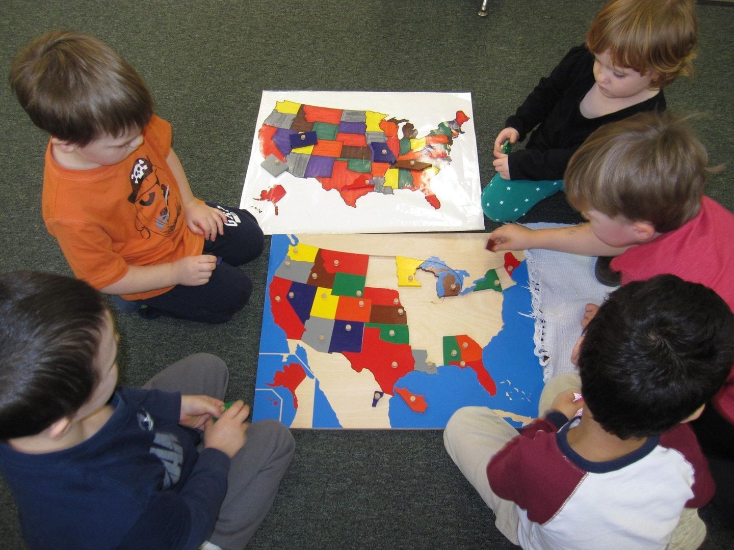 Children around two United States puzzles; some placing pieces, others watching