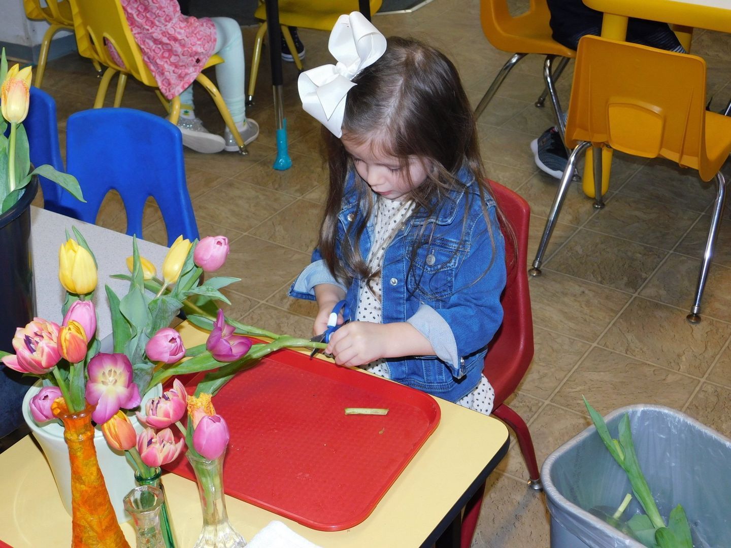 Young girl with a white bow in hair, arranging tulips at a table