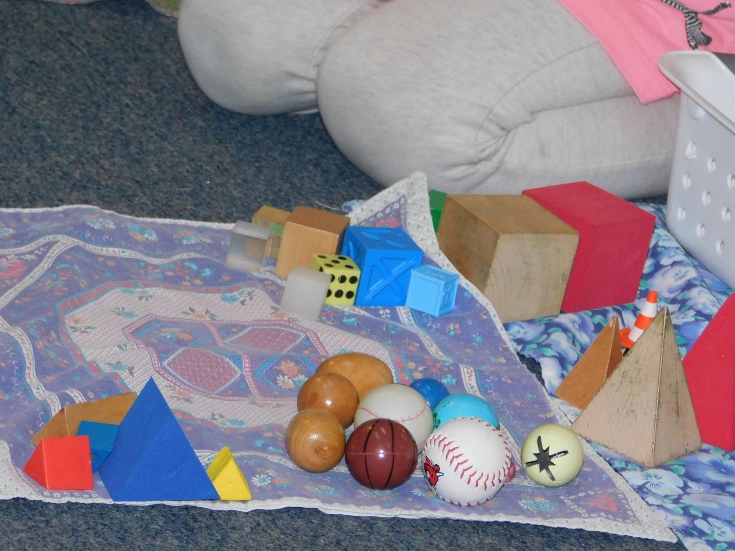 Child's play area with diverse geometric shapes, including cubes, pyramids, and balls, on a patterned blanket