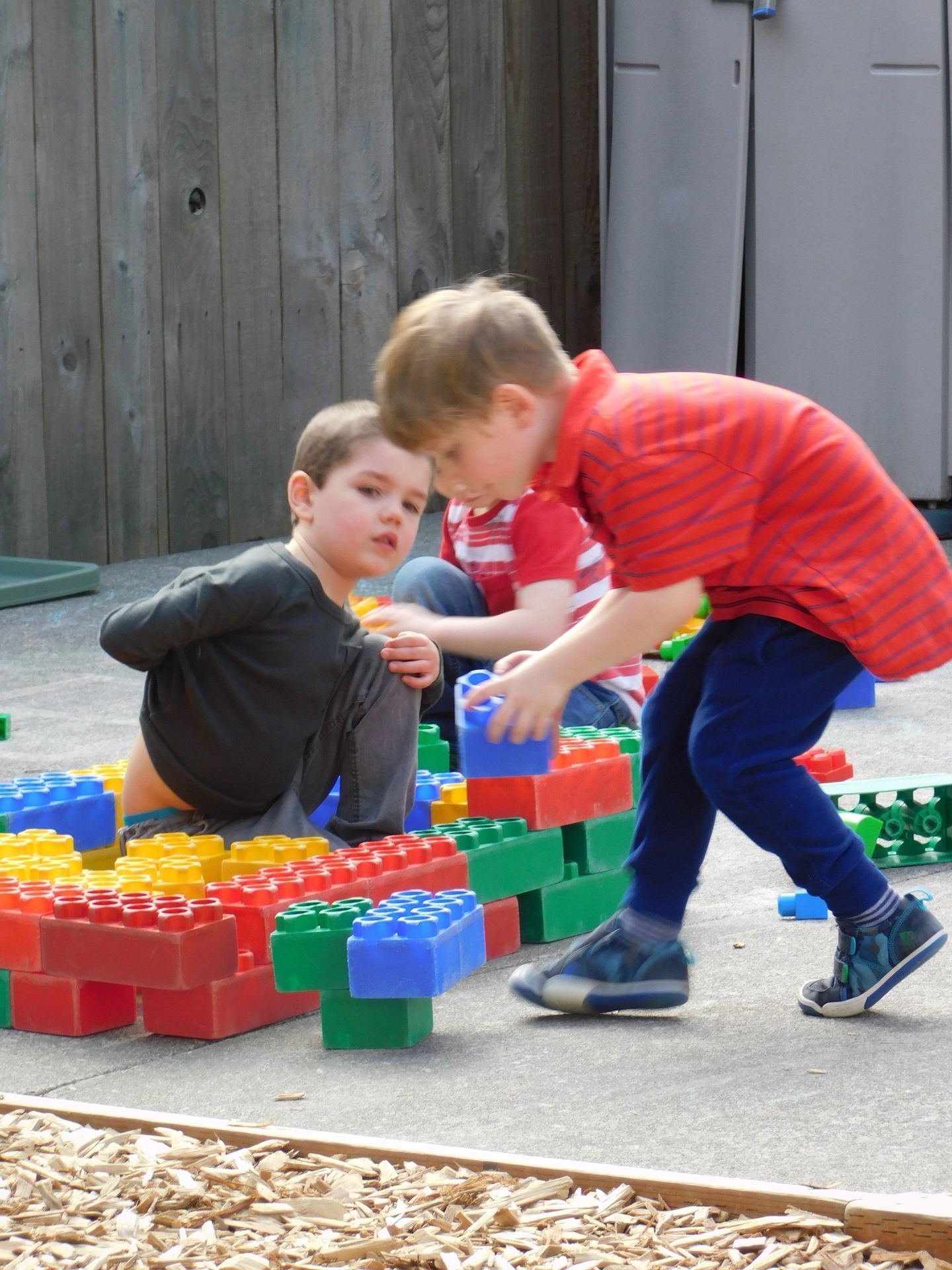Three young children playing with large colorful building blocks outdoors