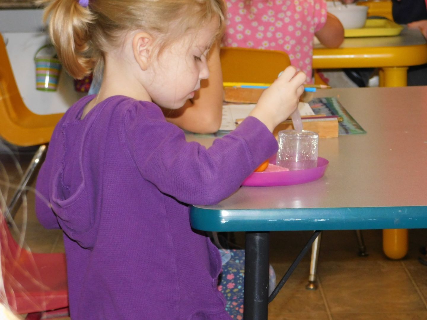 Young girl in purple sweater, playing with ice on a purple plate at a table