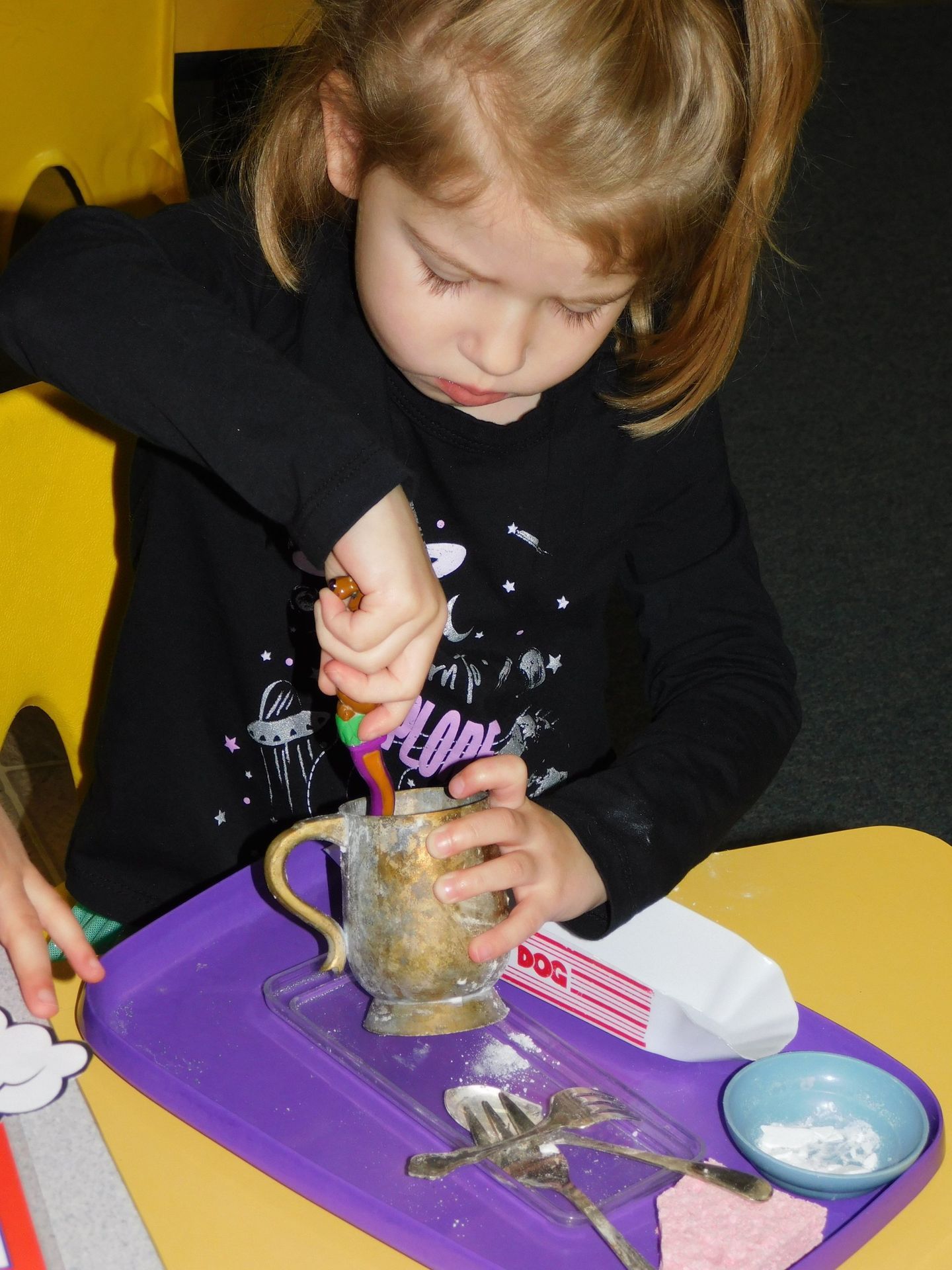 A young girl stirs a metallic cup with a spoon