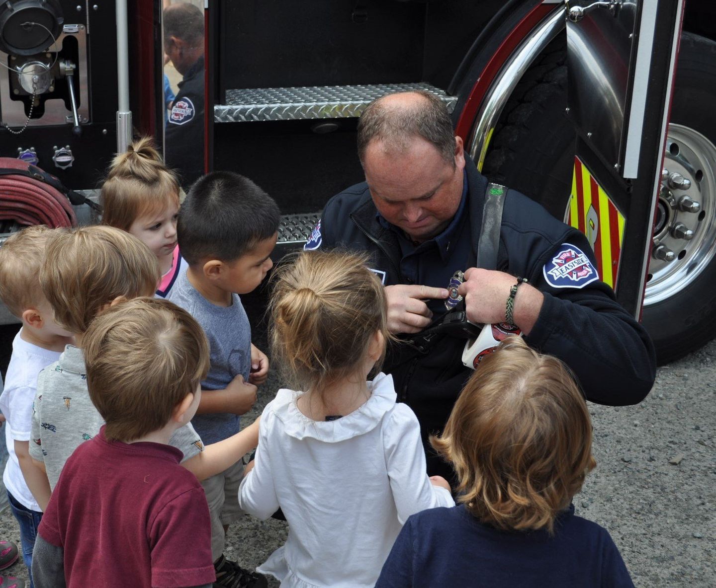 Firefighter shows equipment to a group of children near a fire truck