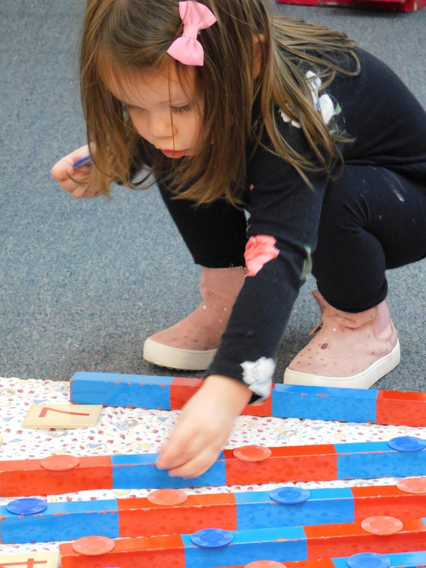 Young girl with pink bow, playing with red and blue blocks on a carpet