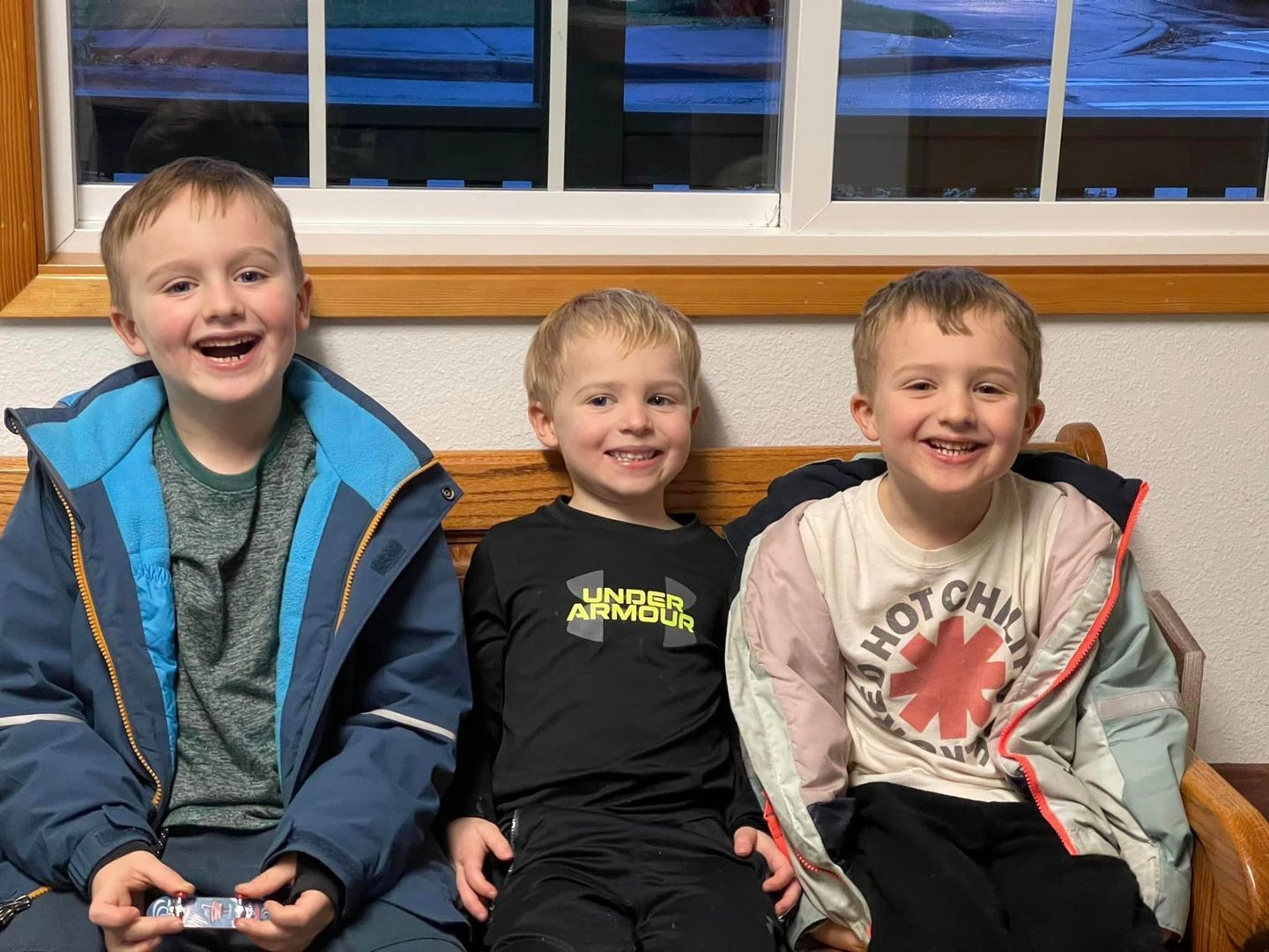 Three young boys smiling and sitting indoors near a window