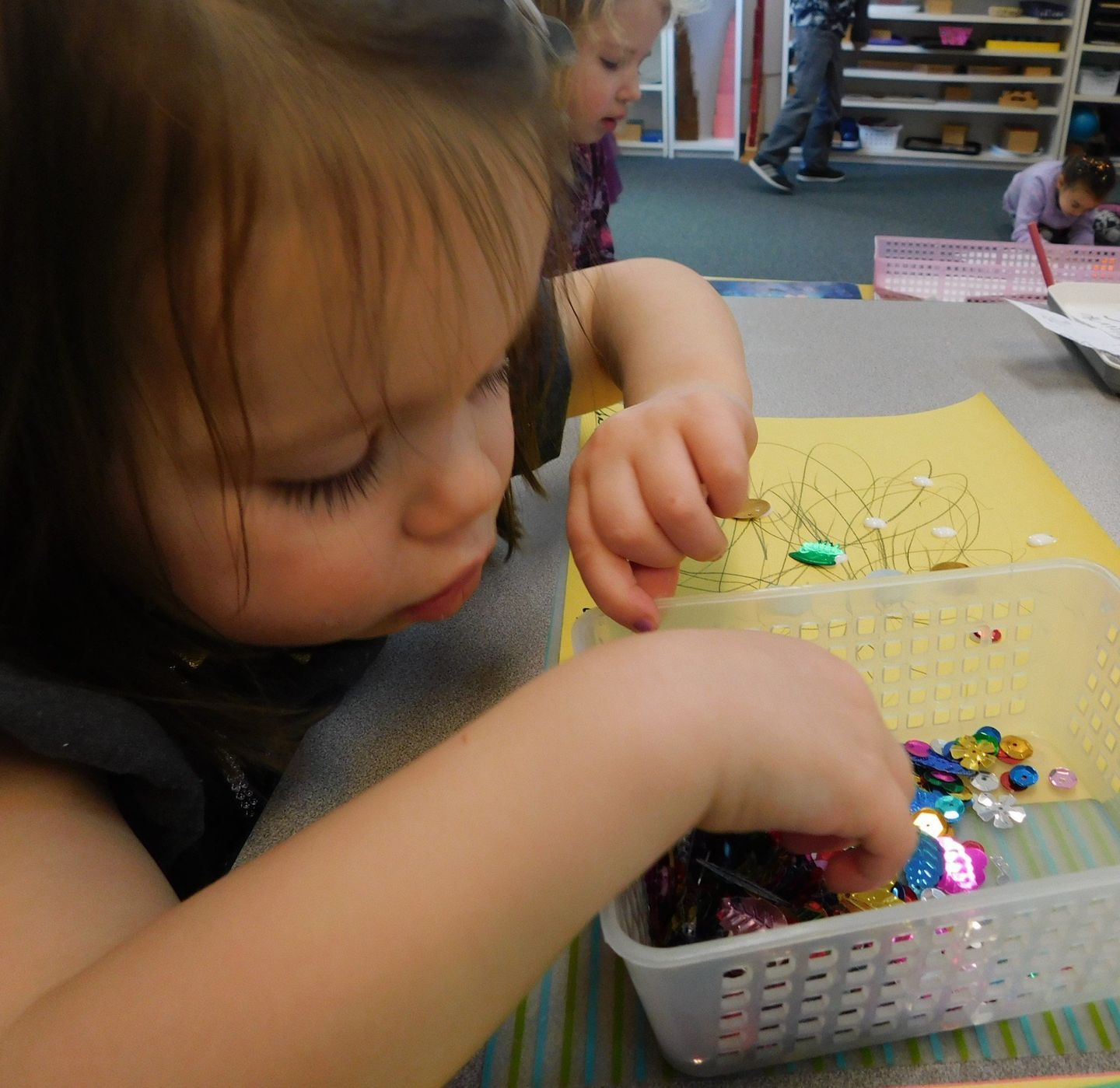 Girl with dark hair looking intently at colorful sequins, selecting them from a container