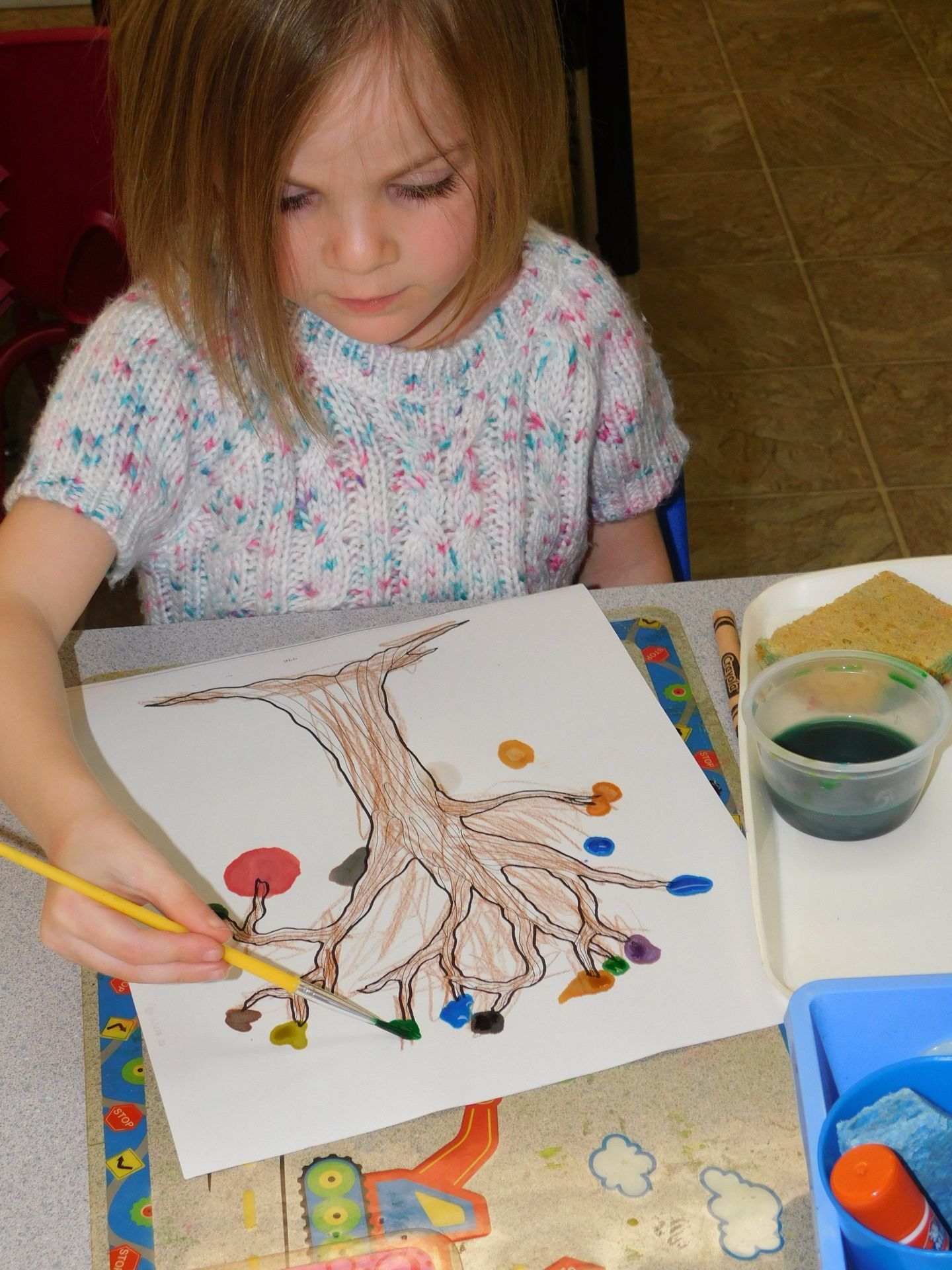 Young girl painting a tree with colorful dots at a table