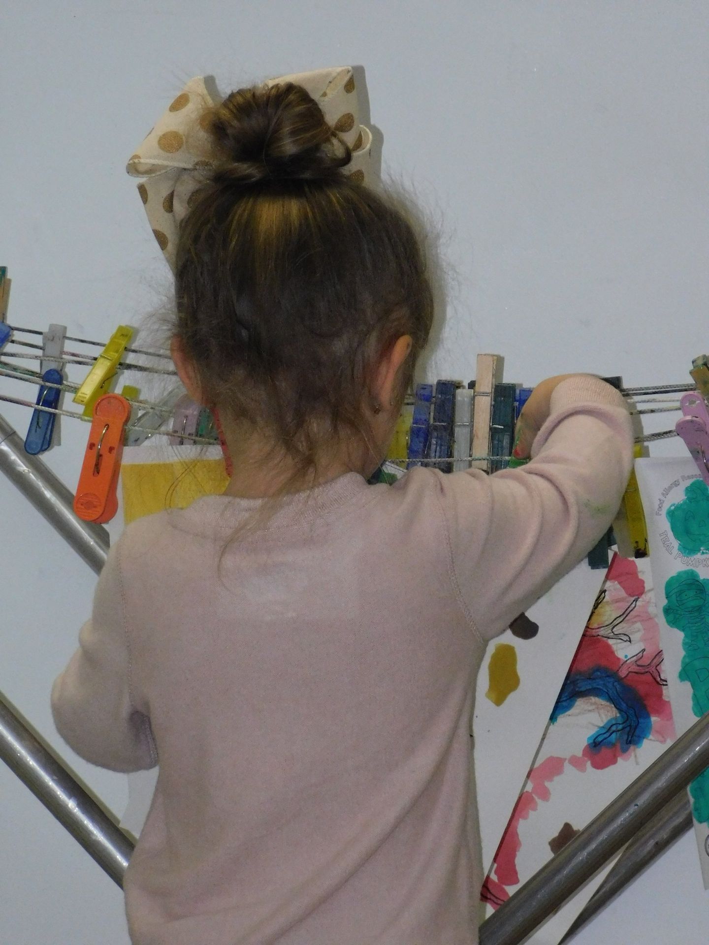 Girl hanging artwork on a clothes drying rack, indoors