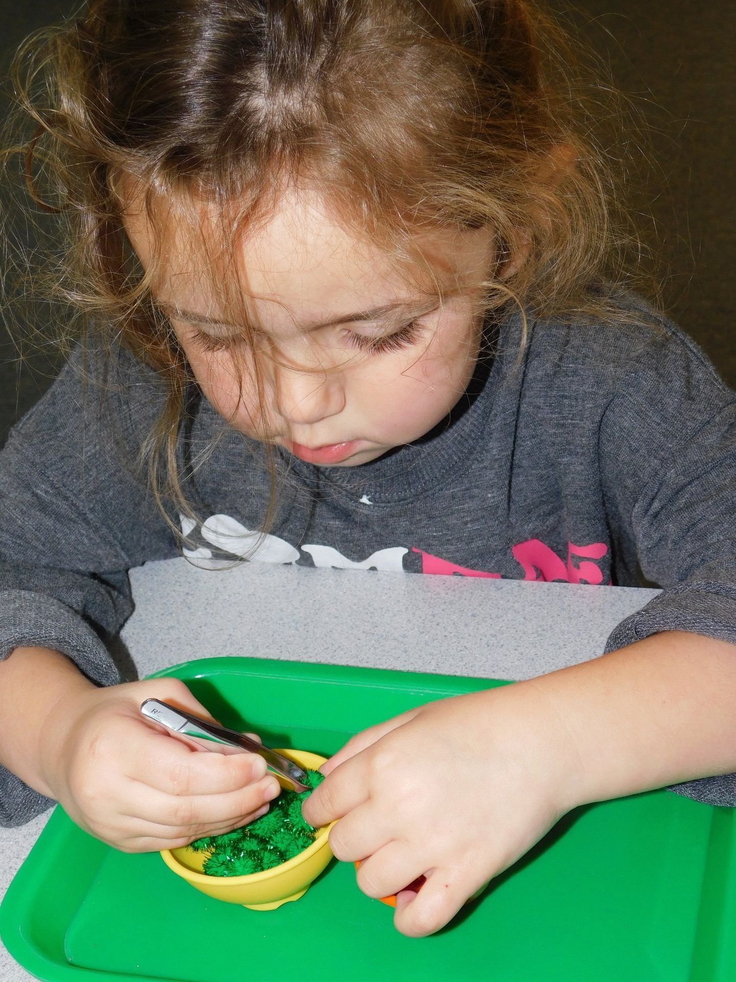 Young child with curly hair focused on playing with green material in yellow bowls