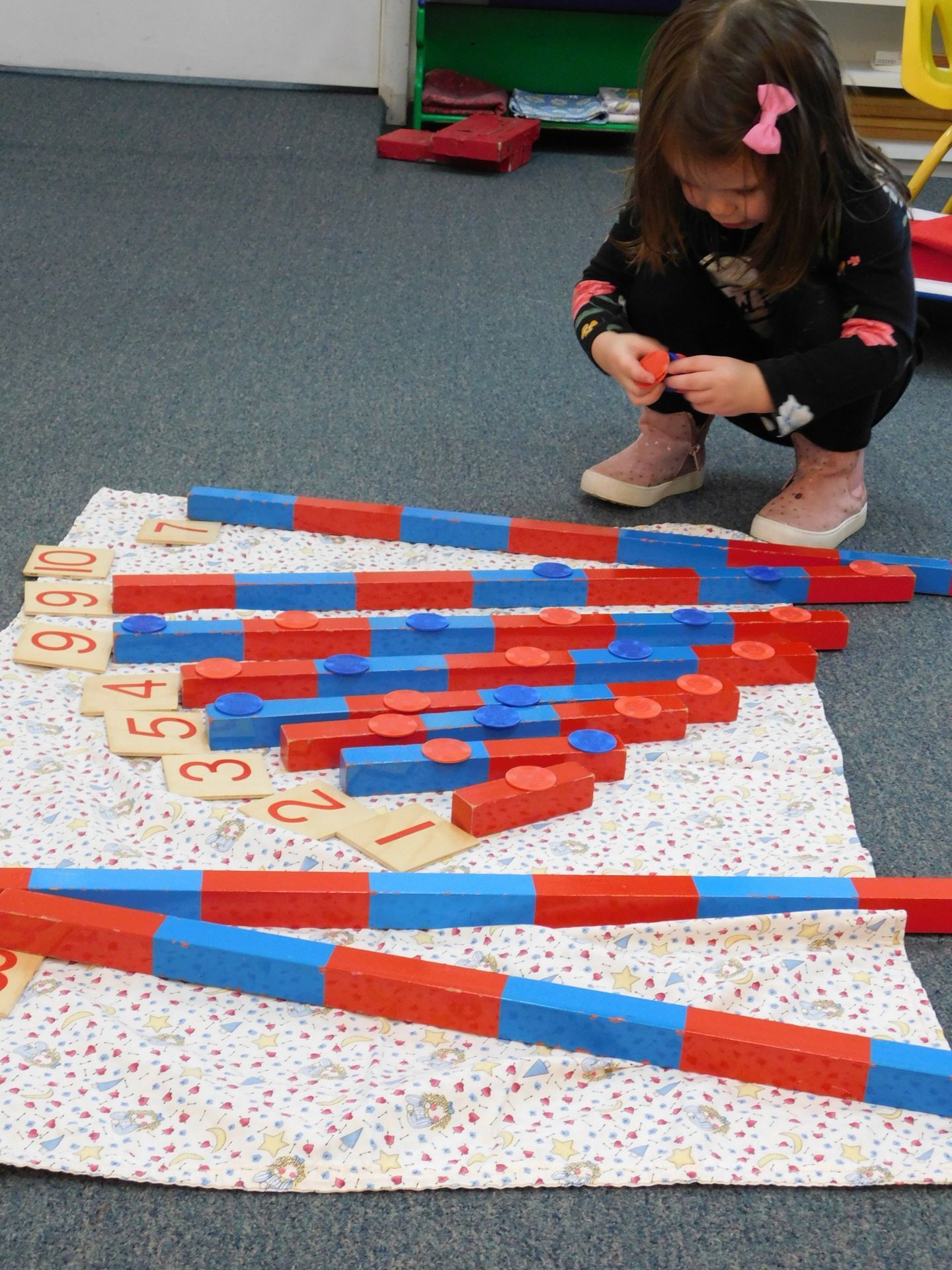 A young girl is playing with colorful wooden number rods on a rug