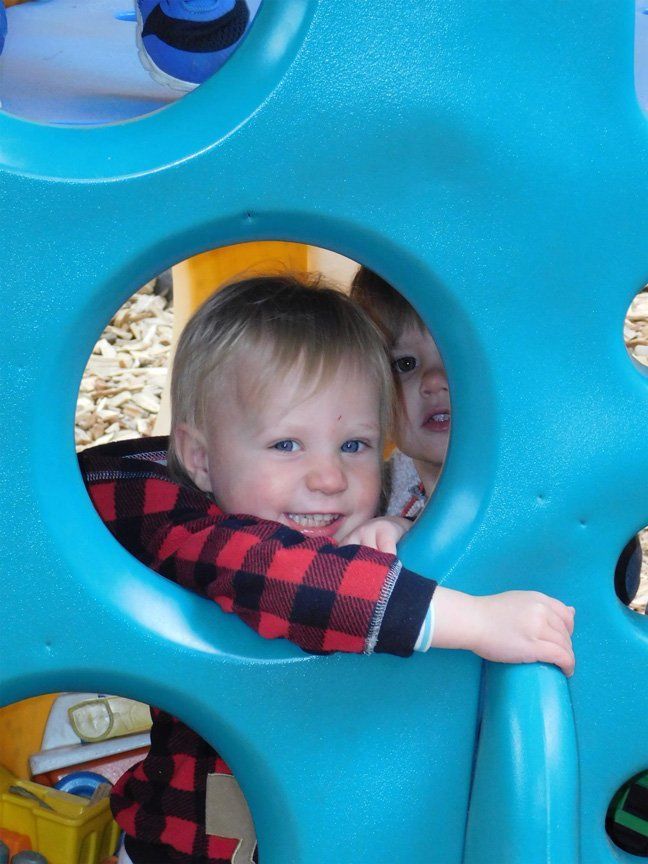 Two young children peering through blue playground structure