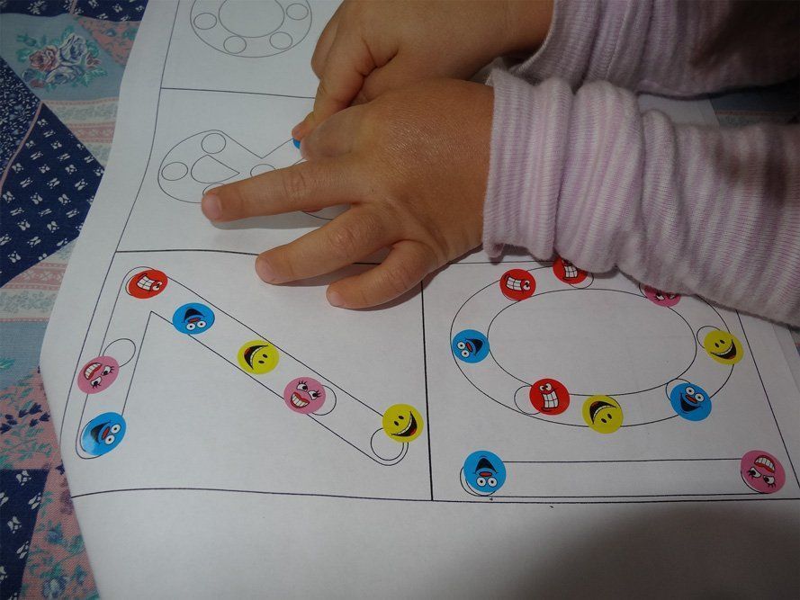 Child's hands tracing a path on a worksheet with colorful smiley faces and shapes