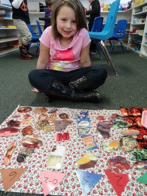 Girl seated on the floor with food cutouts and number cards