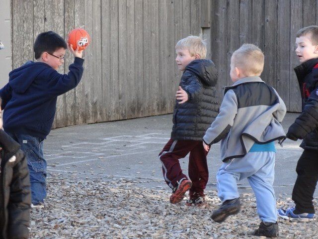 Children playing with an orange ball outdoors near a wooden fence