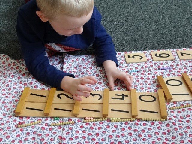 Boy working with number tiles and beads on a patterned mat