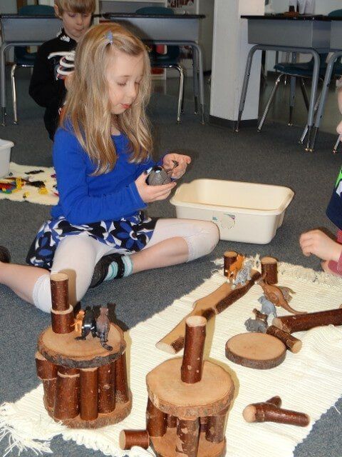 Girl playing with wooden blocks and figurines on a rug in a classroom