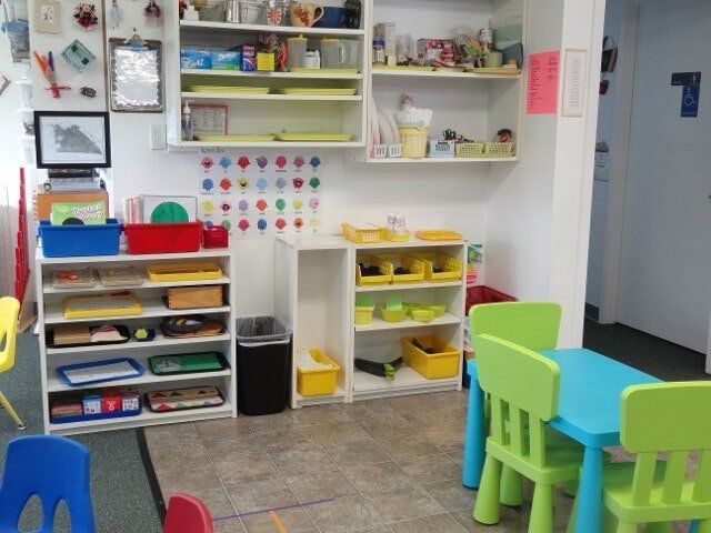 A brightly colored preschool classroom with shelves, tables, and chairs