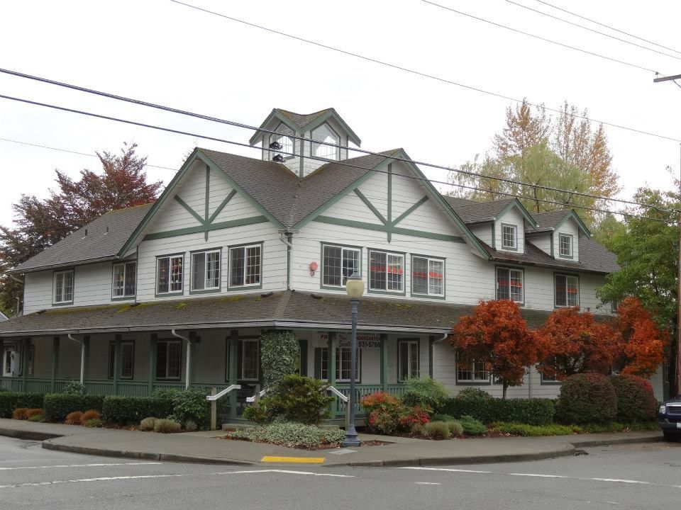 White two-story building with green trim, a porch, and a small cupola; corner lot