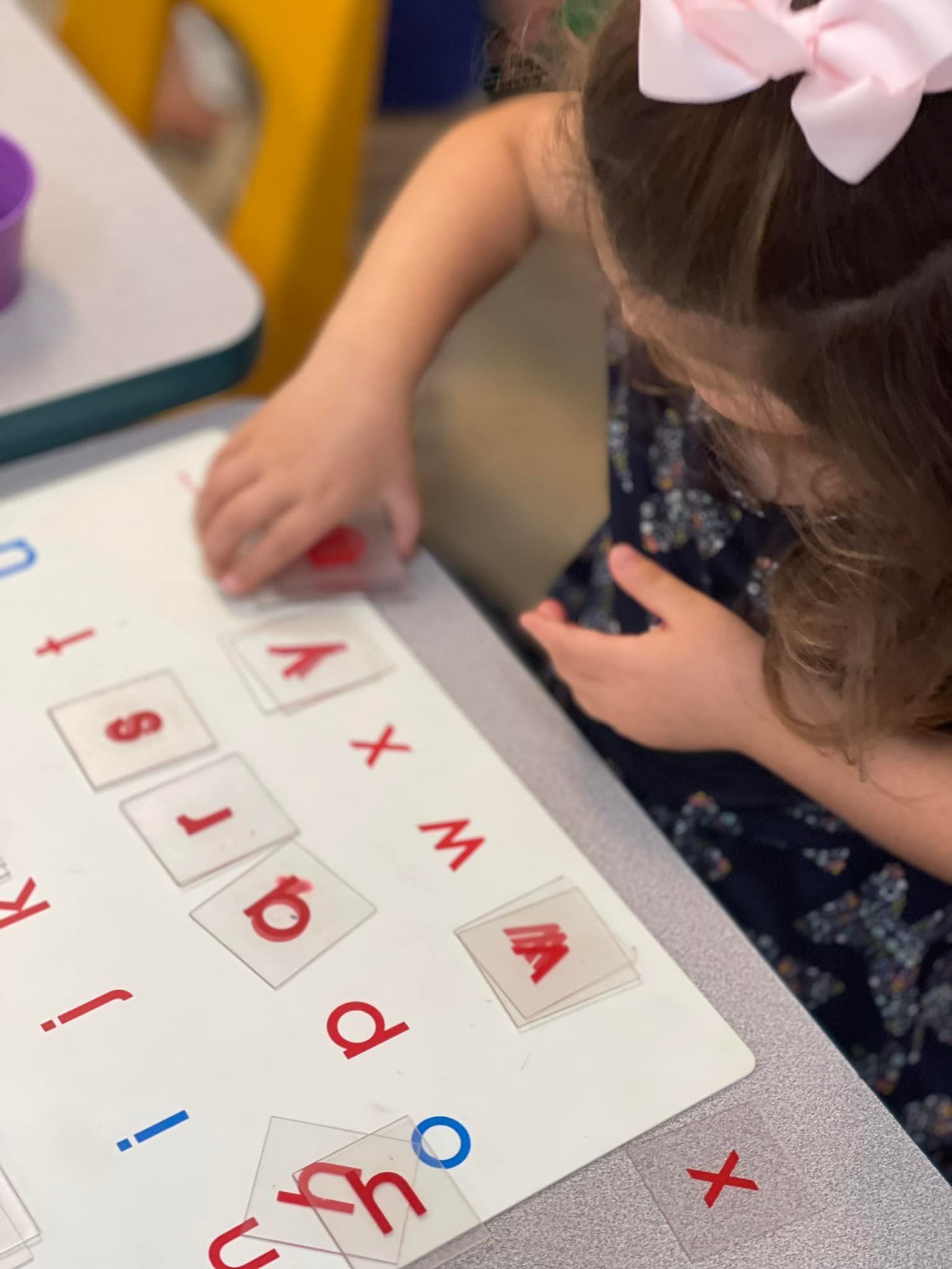 Young girl at a table placing a red letter on a matching lettered card