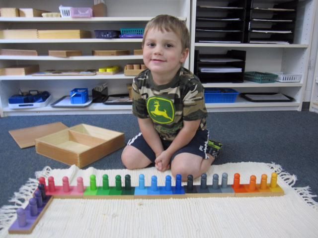 Boy smiles, kneeling with colorful Montessori materials