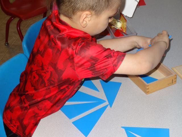 A young child in a red shirt is arranging blue triangles on a white table