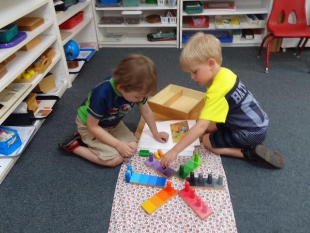 Two young boys on the floor playing with colorful toy blocks and drawing in a classroom