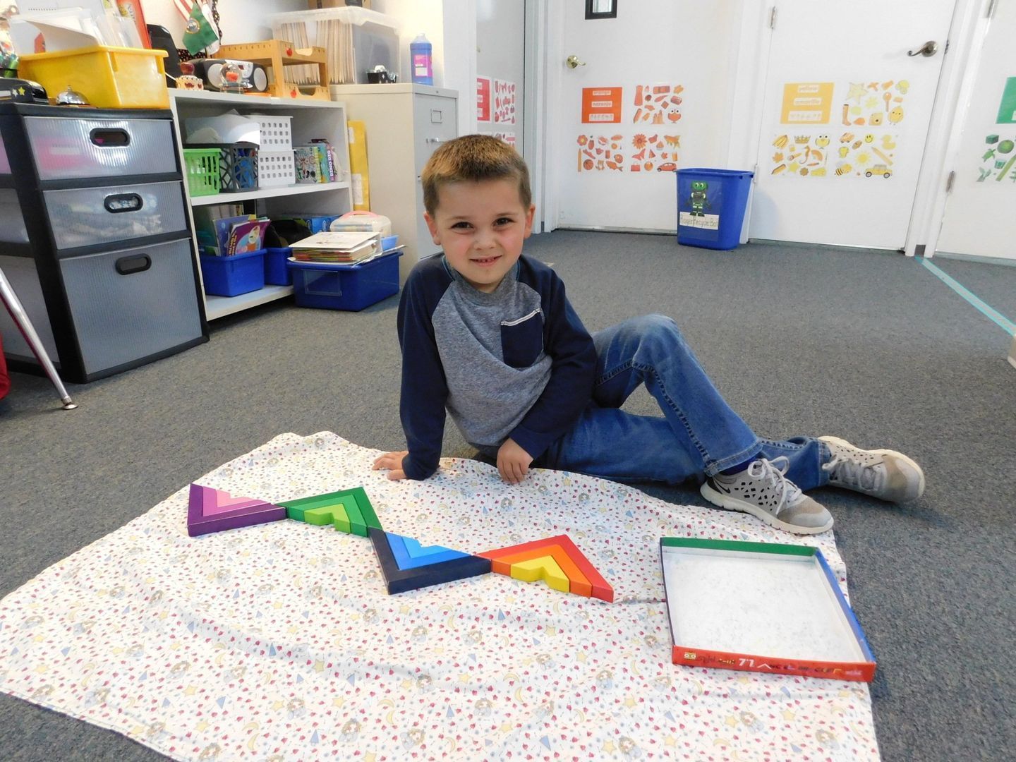 Boy sits with colorful geometric shapes on a blanket in a classroom