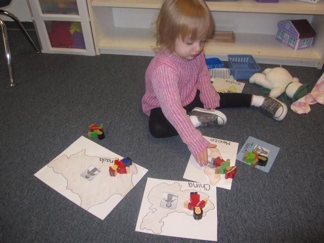 A young child playing with maps on the floor, pointing at one