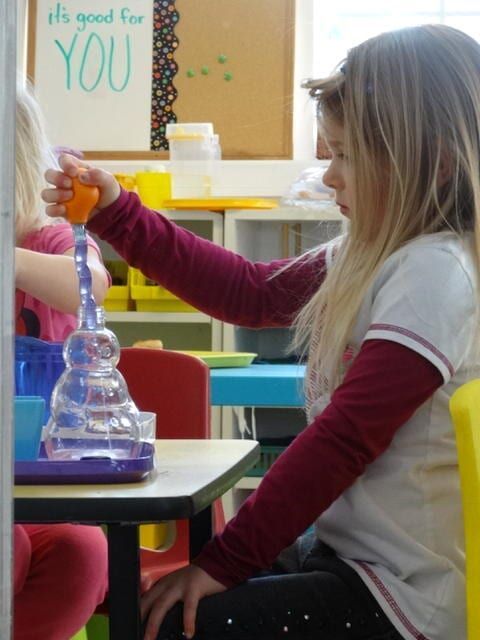 Girl in a classroom playing with a science toy, holding a dropper