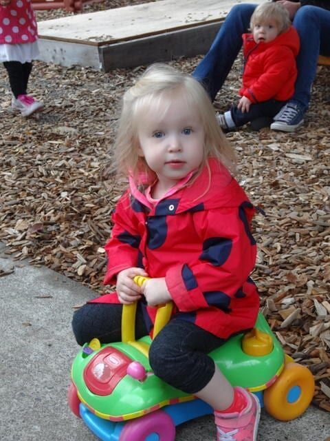 Blonde toddler in red jacket rides a toy car