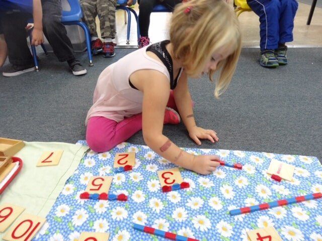 Girl on floor arranging numbers and counting rods.