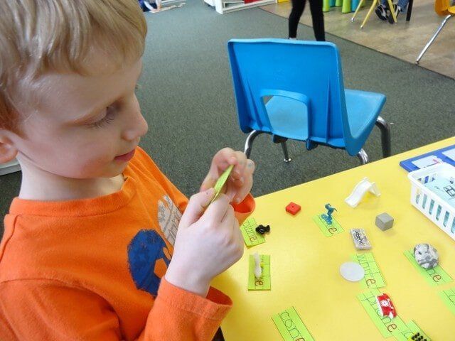 Boy in orange shirt working at a table with toys and labels