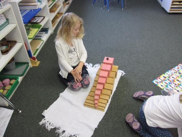 A young girl sits on a rug, using pink and brown blocks in a Montessori setting