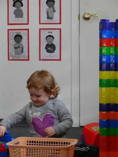 A toddler with red hair smiles while playing with blocks near a colorful tower and a basket