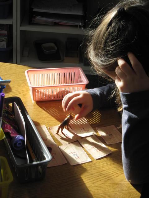 Child playing with toy horse and cards on a table near a pink basket and pencils