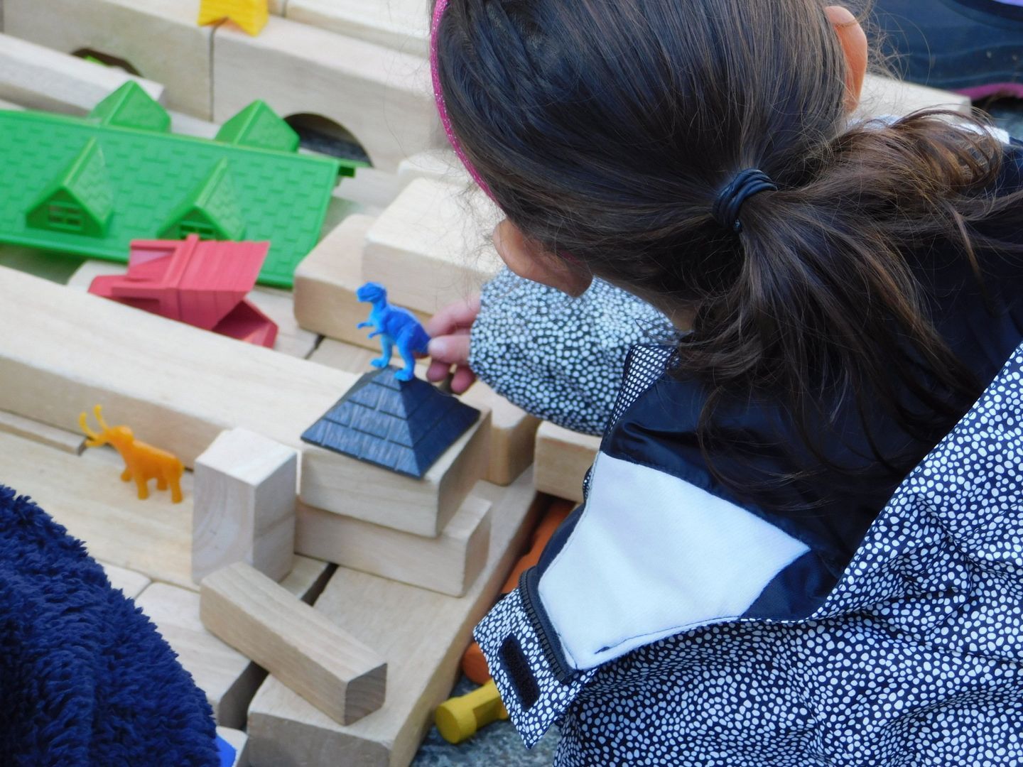 Girl playing with wooden blocks and toy dinosaurs
