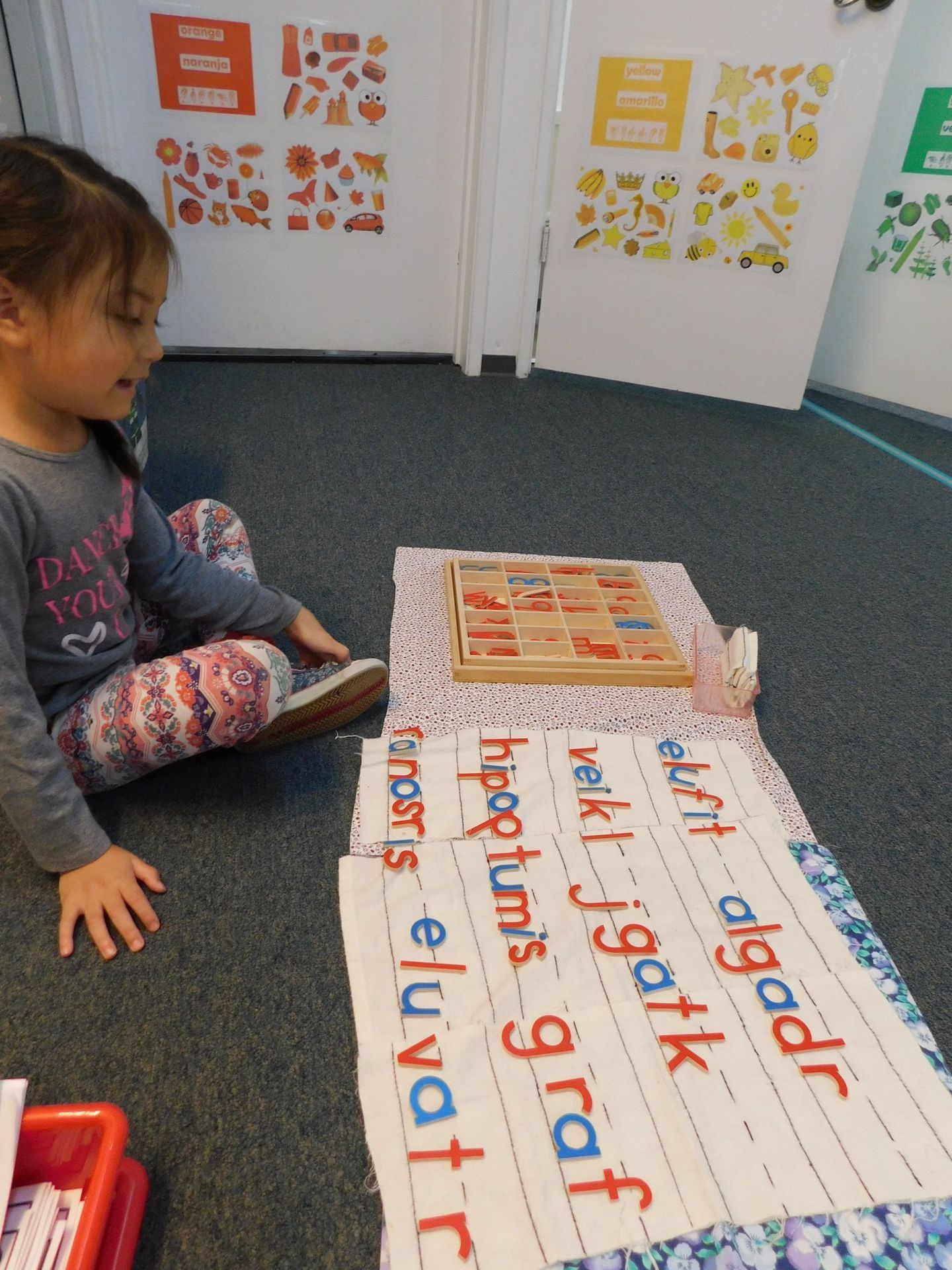 A young girl is using wooden letter tiles and a cloth mat with words on the floor