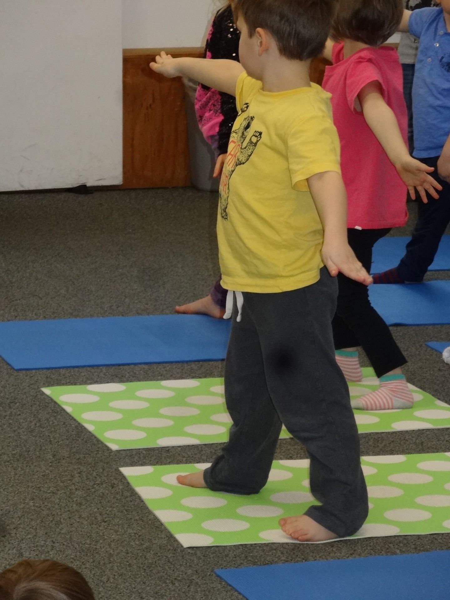 Boy in yellow shirt practices yoga on a mat with other children