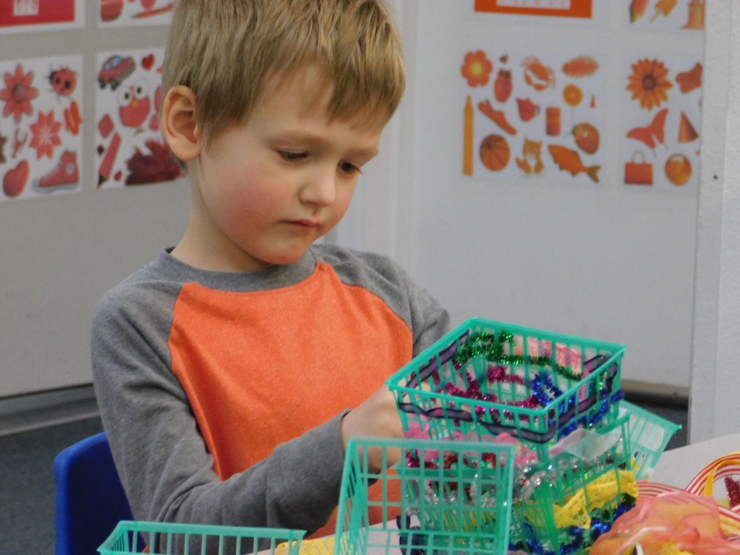 A young boy with light hair builds with small, green plastic baskets at a table