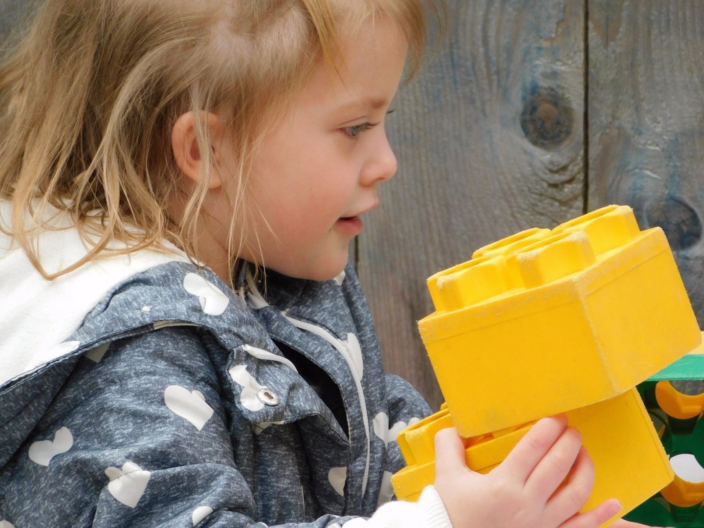 Young child with blonde hair holds large yellow building blocks