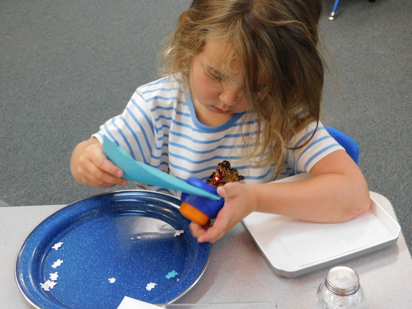 Girl using a blue scoop to pour objects into an orange container