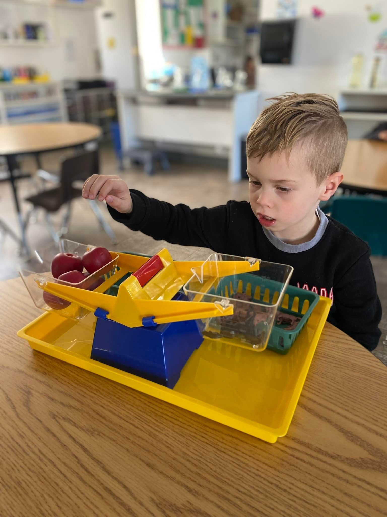 Boy using a balance scale to weigh objects in a classroom