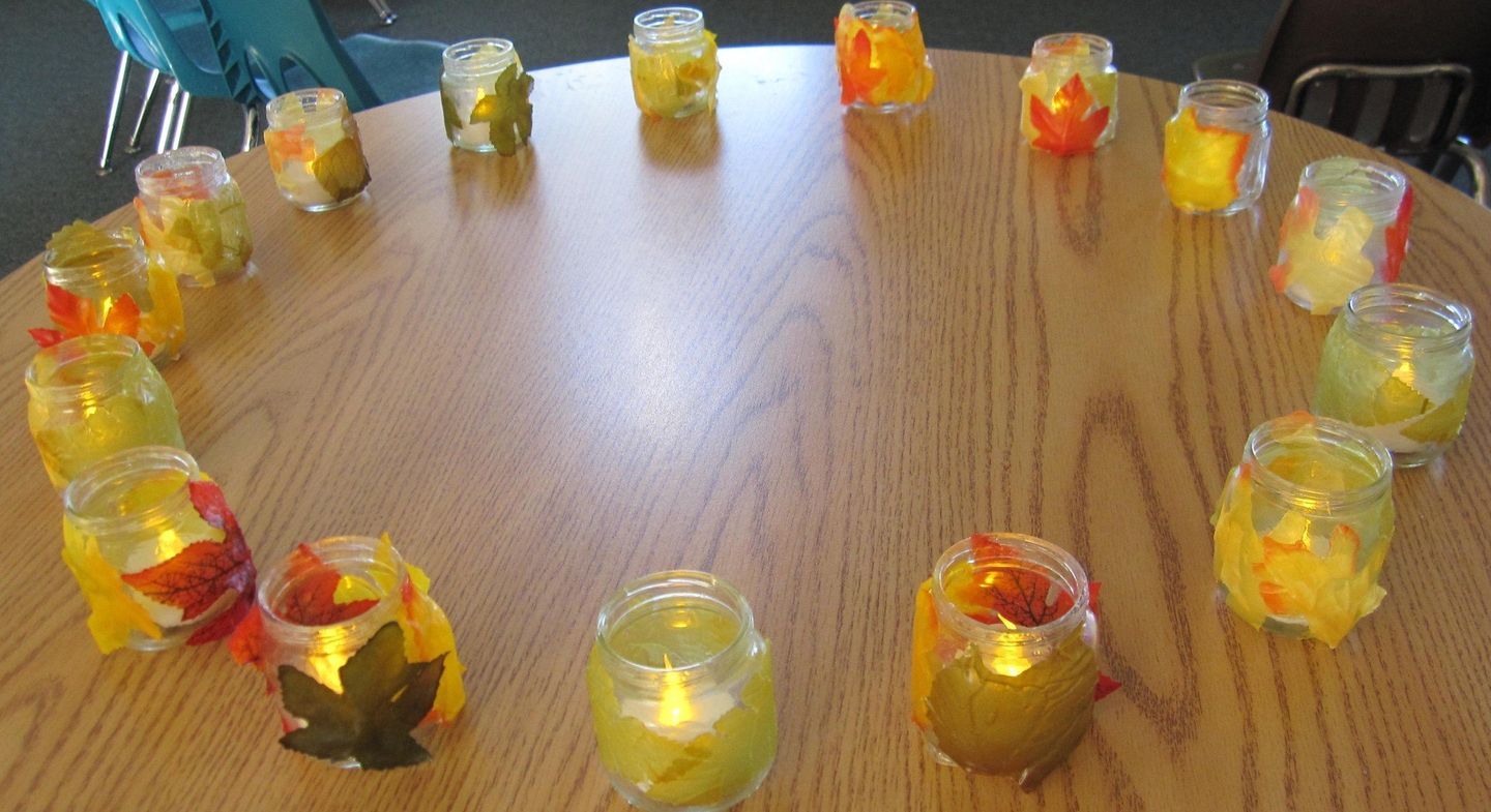 Circle of lit mason jars decorated with fall leaves on a wooden table