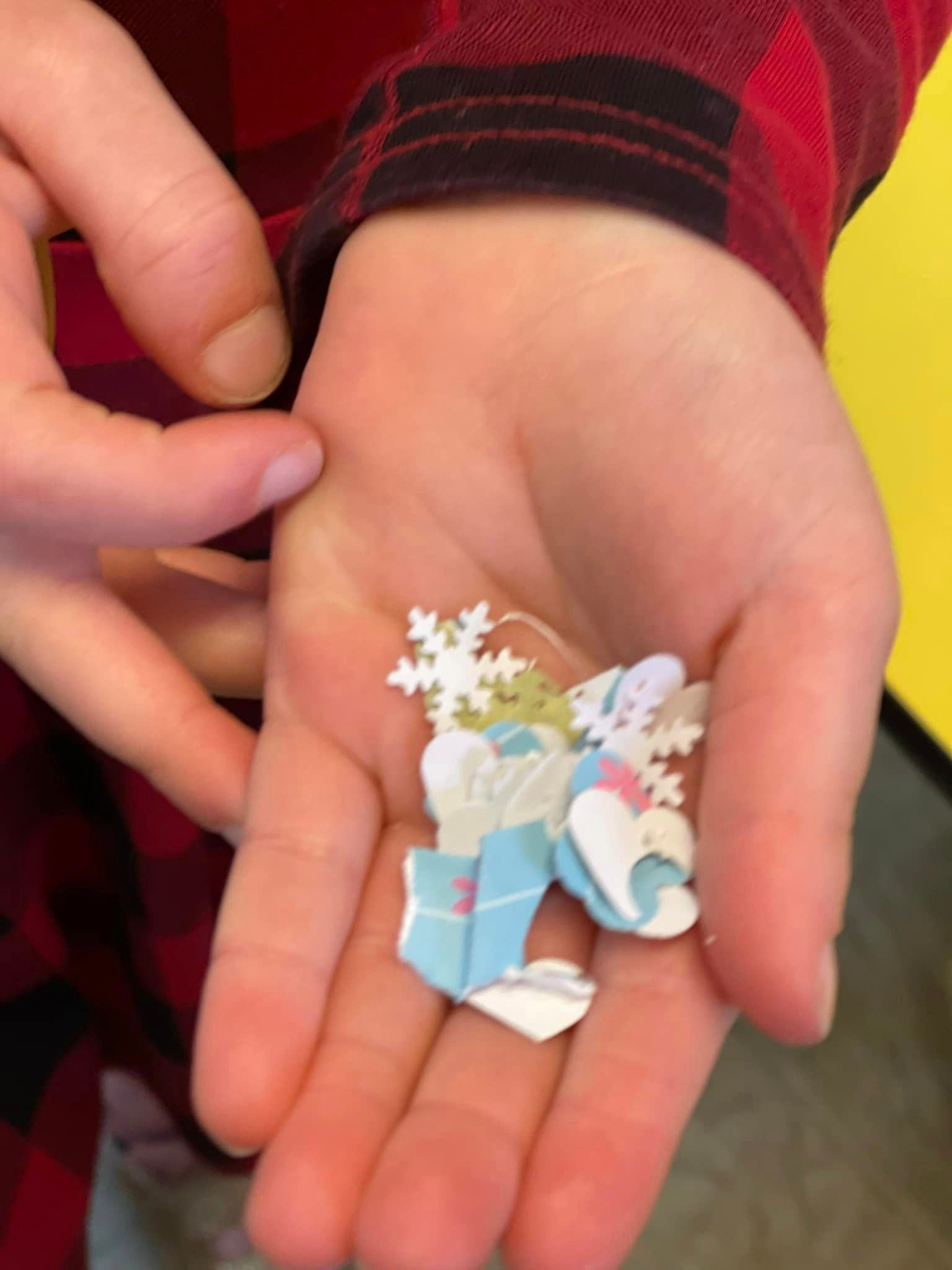Child's open hand holding small, colorful paper cutouts of snowflakes and presents