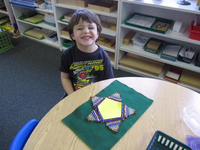 Boy smiles at table with colorful star-shaped craft on green felt in classroom