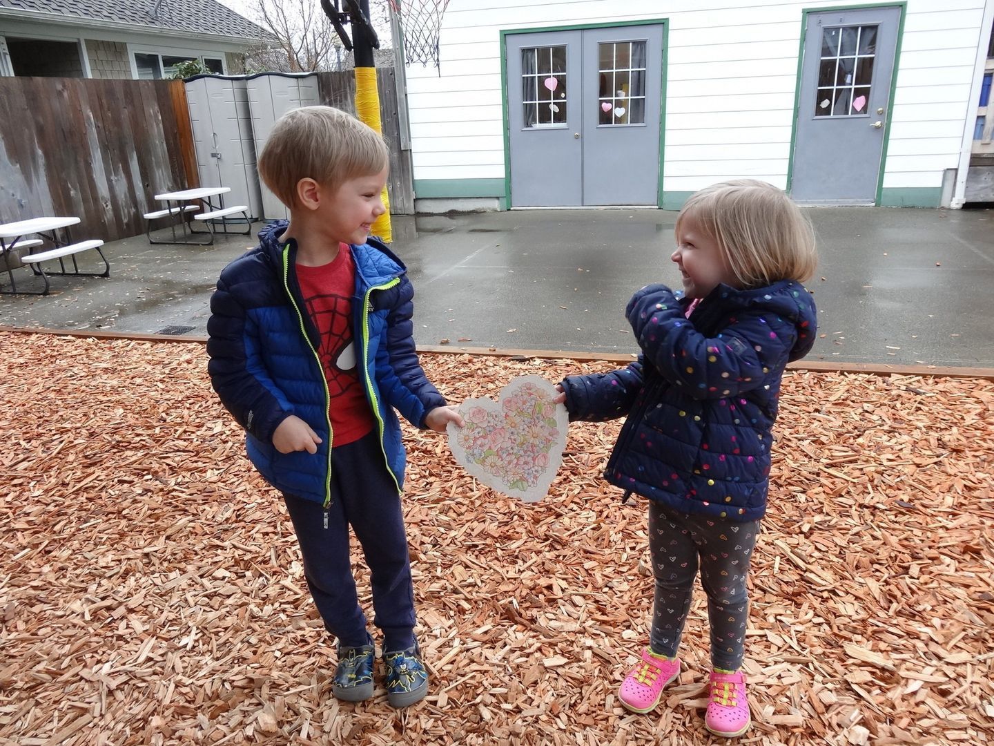Two children holding a heart-shaped craft on a playground.